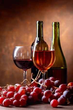 Glasses and bottles of wine on a table with grapes .の写真素材