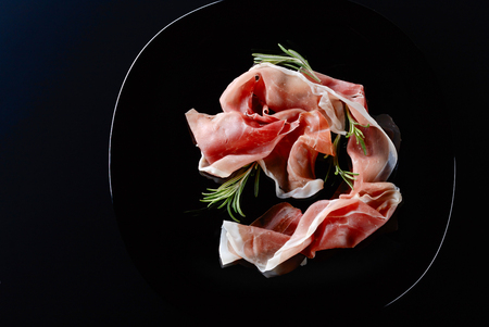 Prosciutto with rosemary on a black plate . Top view.の写真素材