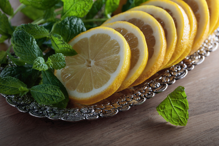 Lemon slices with mint leaves in old silver dish on a wooden table.の写真素材