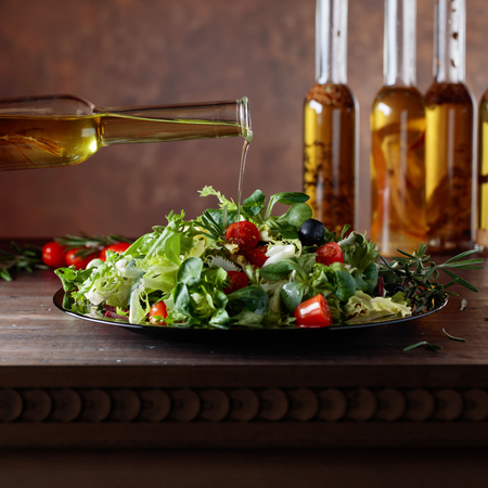 Vegetable salad with olive oil pouring from a small bottle. Old wooden table and brown background. Copy space.の写真素材