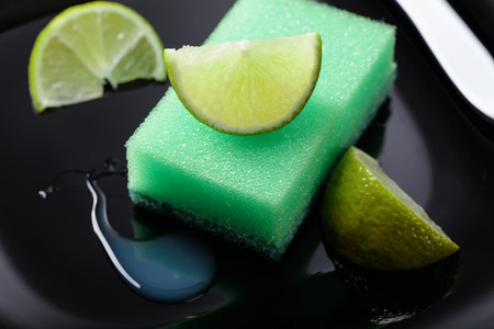 Black plate and dish sponge . Lime slices . Conceptual image on the theme of purity and freshness .