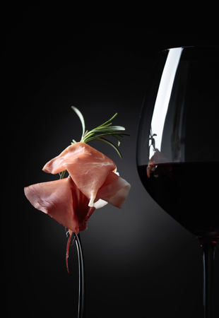 Glass of red wine with prosciutto and rosemary on a black background.の写真素材