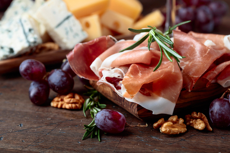 Prosciutto with various cheeses , grapes and  walnuts on a old wooden table.の写真素材