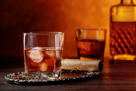 Glass of scotch whiskey with natural ice and cigar on old wooden table.の写真素材