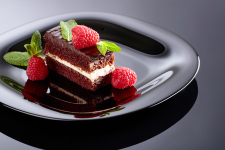 Chocolate cake with raspberry and mint on a black plate.の写真素材