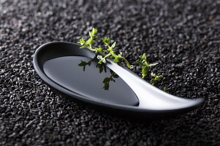 Plant oil in small bowl with thyme branches on a background of black sesame.の写真素材