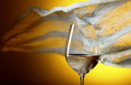 Glass of white wine on a yellow background. Yellow sheer fabric flutters in the wind. Copy space.の写真素材