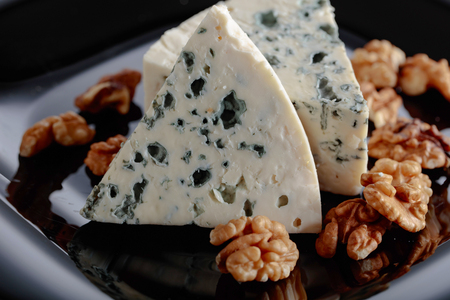 Wedges of soft blue cheese with walnuts on a black plate. の写真素材