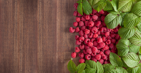 Ripe juicy red raspberries with green leaves on wooden board.Top view ,  copy space.