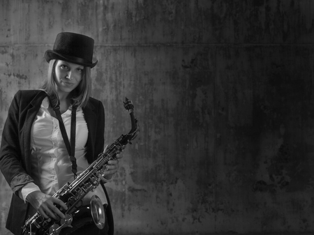 Young beautiful long haired blonde in black hat with saxophone. Black and white , copy space .の写真素材