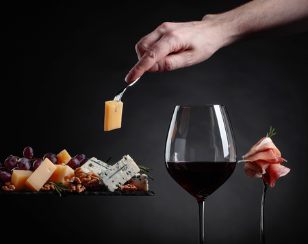 Glass of red wine with various cheeses , fruits and prosciutto on a black background.の写真素材