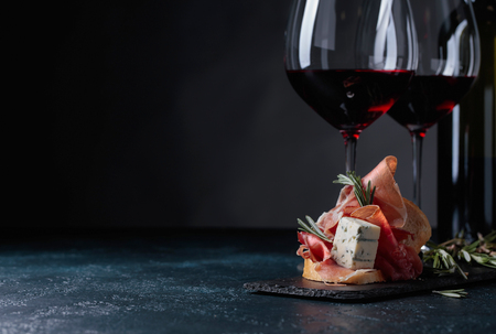 Delicious snack and glasses of red wine. Sandwich with prosciutto, blue cheese and rosemary on a dark background.  Copy space for your text.
の写真素材