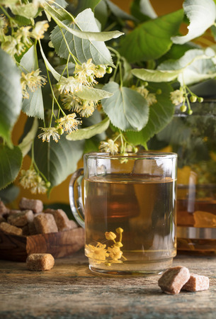Glass of linden tea with brown sugar and flowers on wooden table.の写真素材