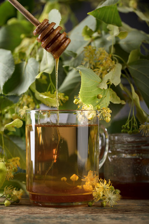 Glass of linden tea with honey and flowers on wooden table.の写真素材