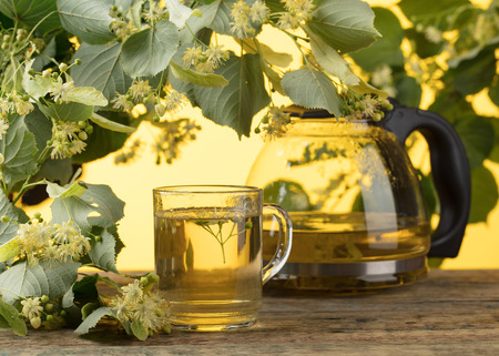 Glass with linden tea and flowers on wooden table.の写真素材