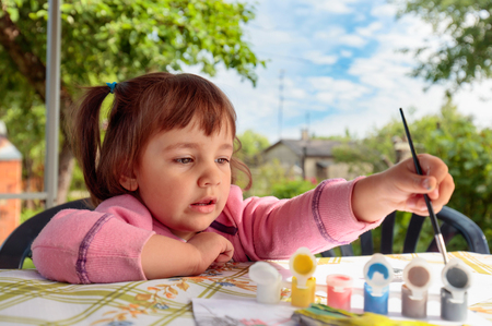 Cute little girl paints animal figures. Summer sunny day in the garden.の写真素材