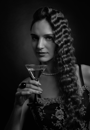 Portrait of a beautiful woman with perfect long hair and makeup .Attractive girl with  glass of martini on a black background . Studio shot .の写真素材