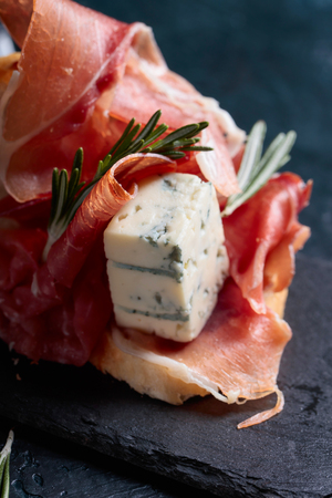 Sandwich with prosciutto, blue cheese and rosemary on a dark background.の写真素材