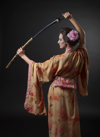 Beautiful woman in traditional Japanese kimono with katana on a black background. Young beautiful woman with perfect hair and makeup. Free space for your content.の写真素材