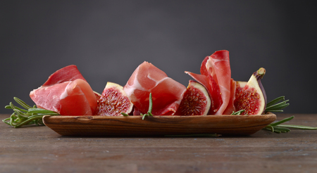 Prosciutto with figs and rosemary on a old wooden table.の写真素材
