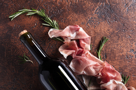 Prosciutto with rosemary and bottle of red wine. Top view, copy space.の写真素材