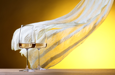 Glasses of white wine on a yellow background. Copy space.  Yellow sheer fabric flutters in the wind. Copy space.の写真素材
