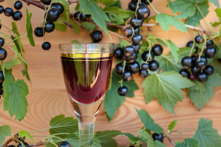 Homemade liqueur made from black currants and fresh berries on a branch , vintage wooden background.の写真素材