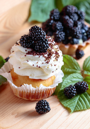 Tasty blackberry cakes with berries and cream on a wooden table.の写真素材