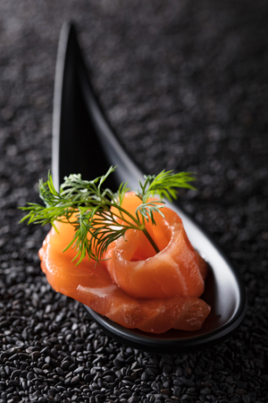 Slice of salted salmon with dill on the background of black sesame.の写真素材