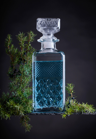 Blue gin in crystal decanter and juniper branch with berries on a black background.の写真素材