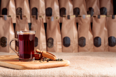 Glass of hot tea. Wooden spoon with dried tea leaves. Craft paper pack with window for loose tea. Copy space.の写真素材
