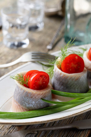 Herring rolls with dill, green onion and cherry tomatoes on a old wooden tableの写真素材