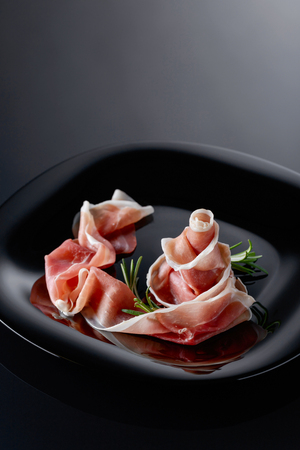 Prosciutto with rosemary on a black plate. Copy space.の写真素材