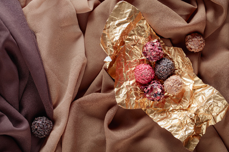 Various chocolates in golden foil on a beige satin. Top view.