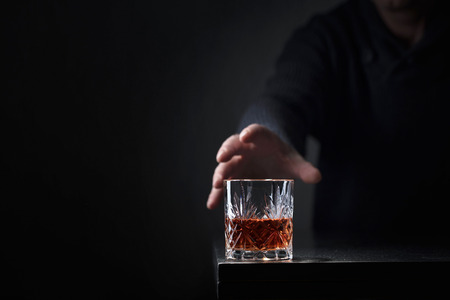 Man's hand reaches for a glass of alcohol. Conceptual image on the subject of alcoholism. Copy space...