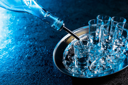 Vodka poured into a glass lit with blue backlight.Chilled vodka with pieces of ice.の写真素材