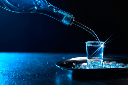 Vodka poured into a glass lit with blue backlight. Copy space.Chilled vodka with pieces of ice.の写真素材
