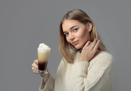 Attractive young woman with Irish coffee. Beautiful blonde in a sweater holding a mug of coffee with cream. Copy space.の写真素材