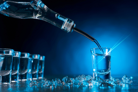 Vodka poured into a glass lit with blue backlight. Copy space.Chilled vodka with pieces of ice.