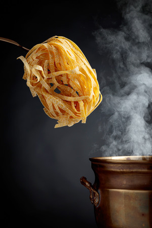 Homemade raw egg noodles and old brass pan with hot water. Black background. Copy space for your text.の写真素材