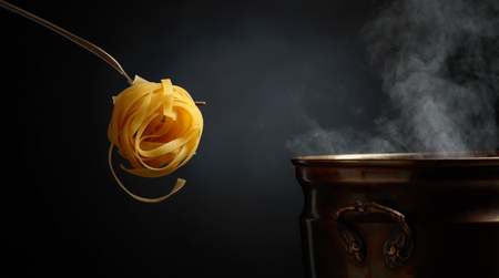 Homemade raw egg noodles and old brass pan with hot water. Black background. Copy space for your text.の写真素材