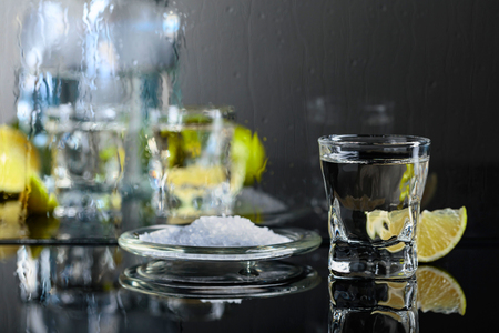 Glass of tequila with lime and salt on the black reflective background. Alcohol in glass before wet glass with water drops.の写真素材