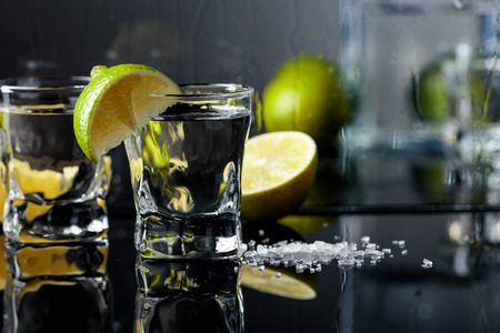 Glasses of tequila with lime and salt on the black reflective background. Alcohol in glasses before...