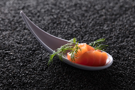 Slice of salted salmon with dill on the background of black sesame.の写真素材