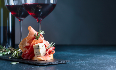 Sandwich with prosciutto, blue cheese and rosemary on a dark background. Glasses and bottle of red wine with snack. Copy space for your text.の写真素材