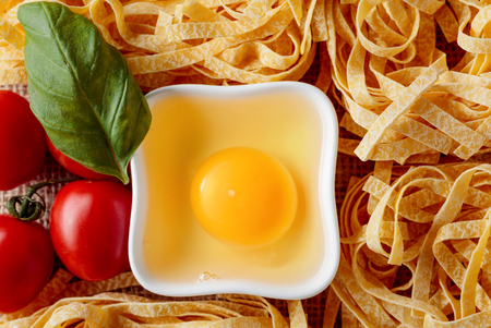 Homemade raw egg noodles with tomato and basil. Top view.の写真素材