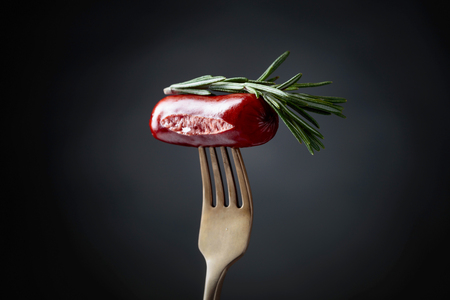 Grilled sausage with rosemary on a fork. Black background, copy space.