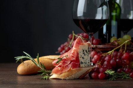 Sandwich with prosciutto, blue cheese and rosemary on a dark background. Delicious snack and red wine. Copy space for your text.の写真素材