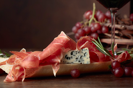 Sandwich with prosciutto, blue cheese and rosemary on a dark background. Delicious snack and grapes. Copy space for your text.の写真素材