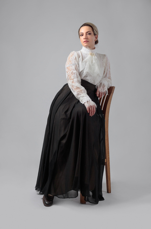 Portrait of a woman in Victorian clothes. White blouse with lace, embroidery and high collar. Long layered skirt with wide belt.の写真素材